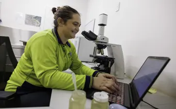 Humpty Doo Barramundi Worker Typing On A Keyboard And Conducting Research With A Microscope In An Office