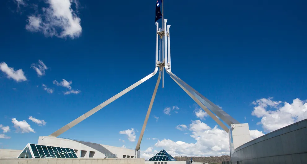 wide angle view of top of Australian Parliament House large tripod flagpole and australian flag on a dark blue sky
