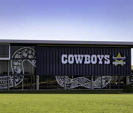 NQ Cowboys Hutchinson Builders Centre Front View Of Exterior With Indigenous Snake Artwork On Glass And Cowboys Logo With Grass In The Foreground on Hutchinson Builders Centre