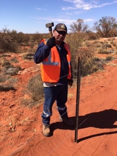 Indigenous worker constructing a wire fence hammering a star picket into the ground